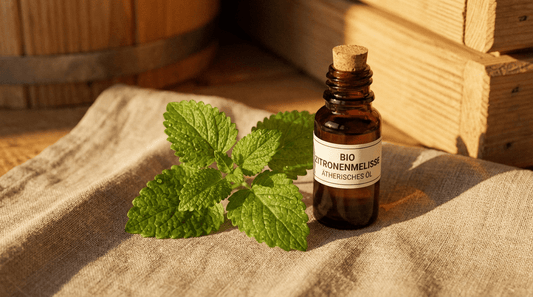 Melisse ätherisches Öl in dunkler Glasflasche neben frischen grünen Melissenblättern auf rustikalem Saunahandtuch – beruhigender zitronig-krautiger Duft für entspannende Saunaaufgüsse am Abend
