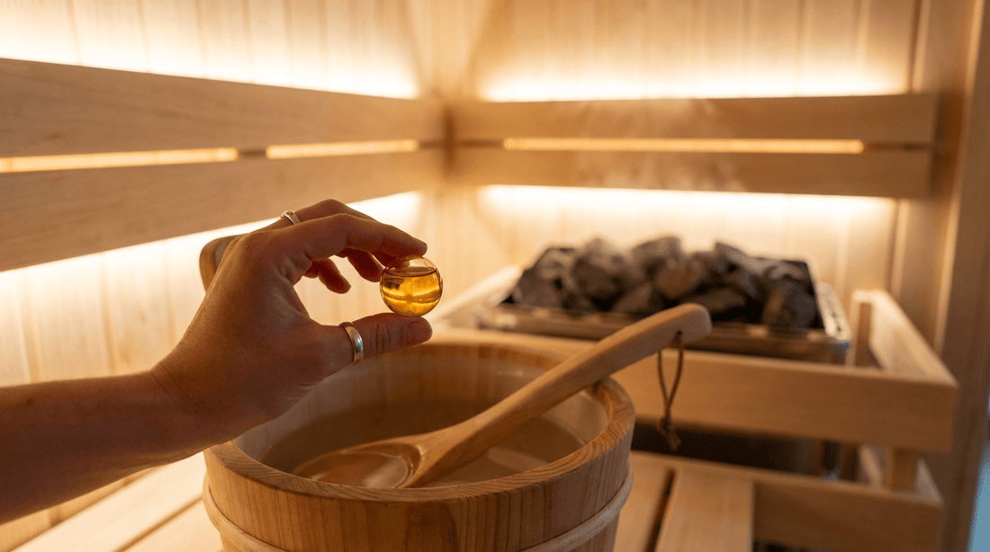 Hand hält einen Saunadrop über einen Holz-Saunaeimer mit klarem Wasser in einer finnischen Sauna