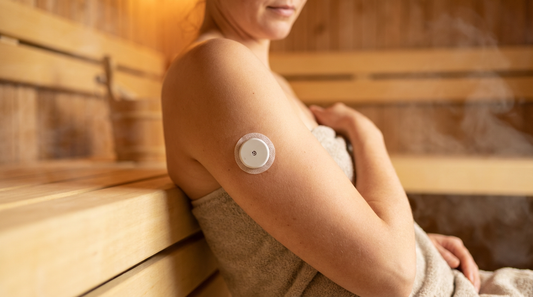 CGM-Glukosesensor am Oberarm einer Person in einer finnischen Holzsauna mit warmem Licht und leichtem Dampf